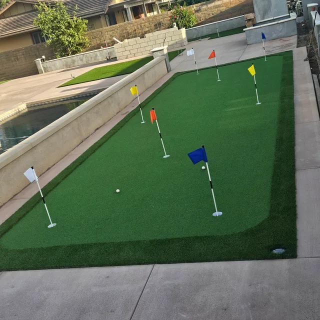 Backyard putting green with colored flags beside a pool and patio