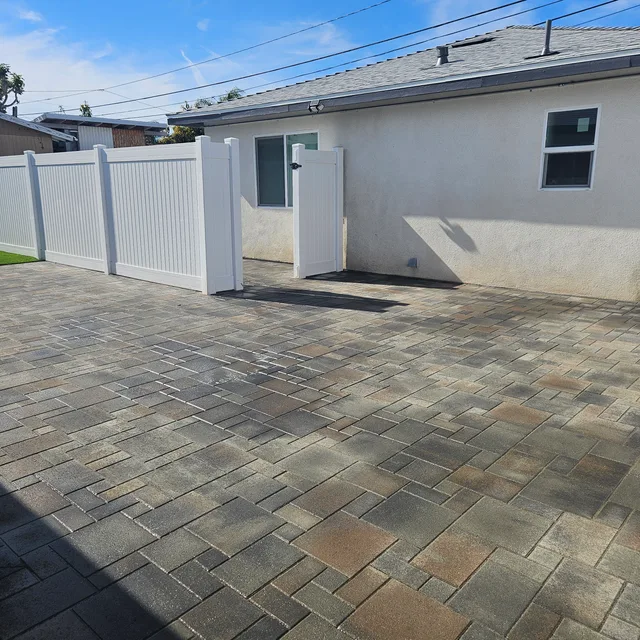 Large paver surface with a staggered pattern beside a white fence and house