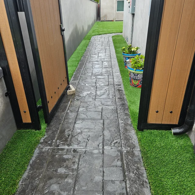 Textured pathway framed by artificial turf through an open wooden gate
